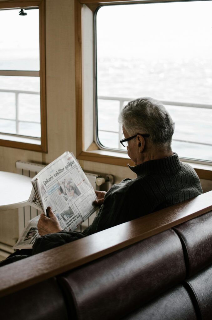 pexels-photo-3393375-3393375 Elderly man reading newspaper inside ferry, enjoying a peaceful travel moment.