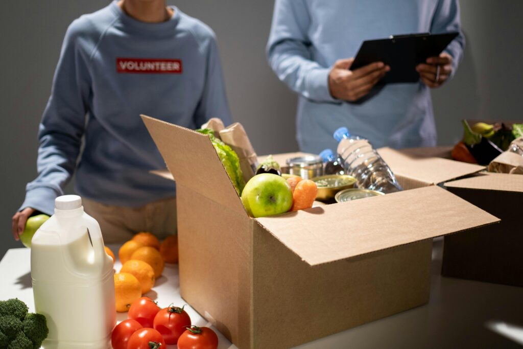 pexels-photo-6590920-6590920 People packing a cardboard box with essentials like fruits, vegetables, and bottled water for charity.