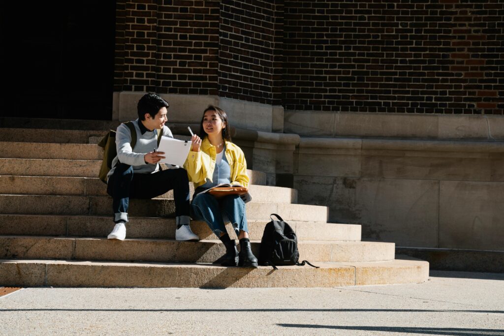 Two college students sitting on steps outdoors studying together in natural light.